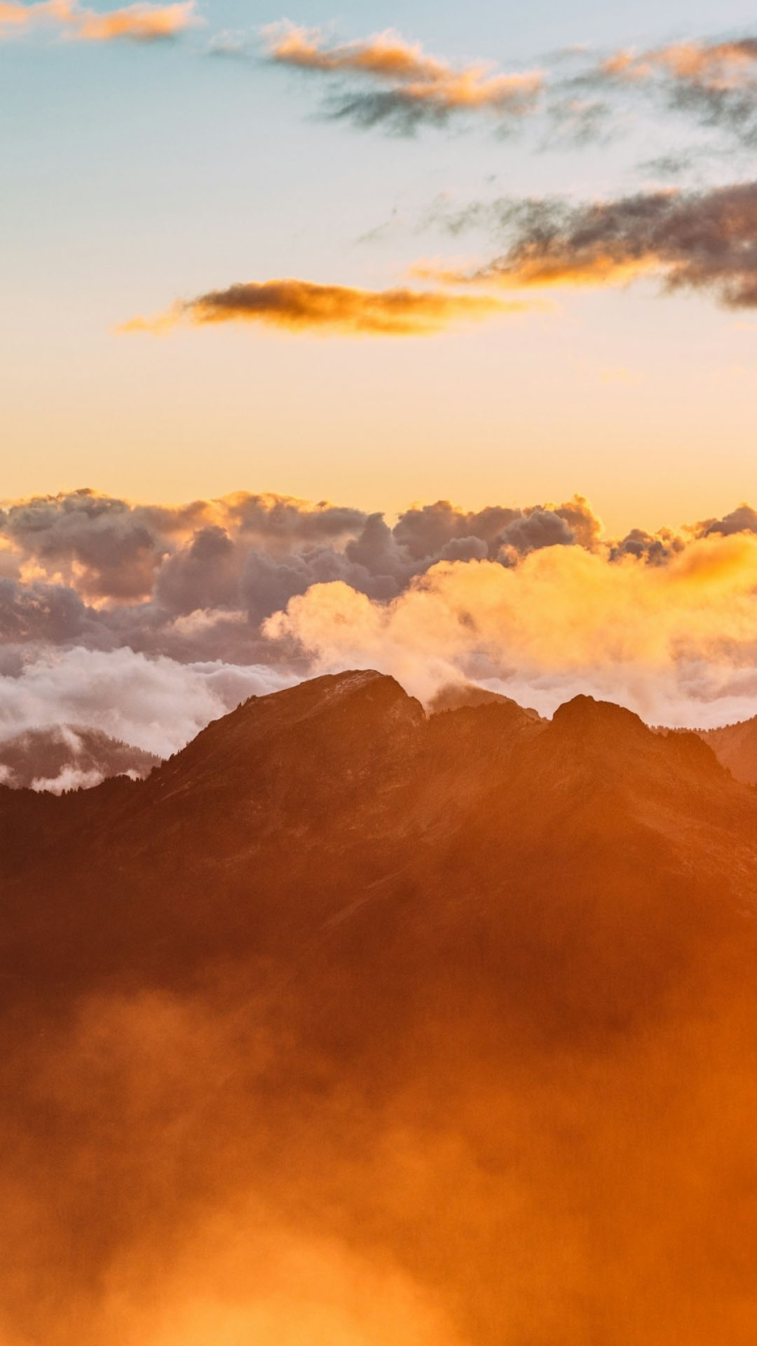 Golden light illuminating clouds and mist over rugged mountain peaks.