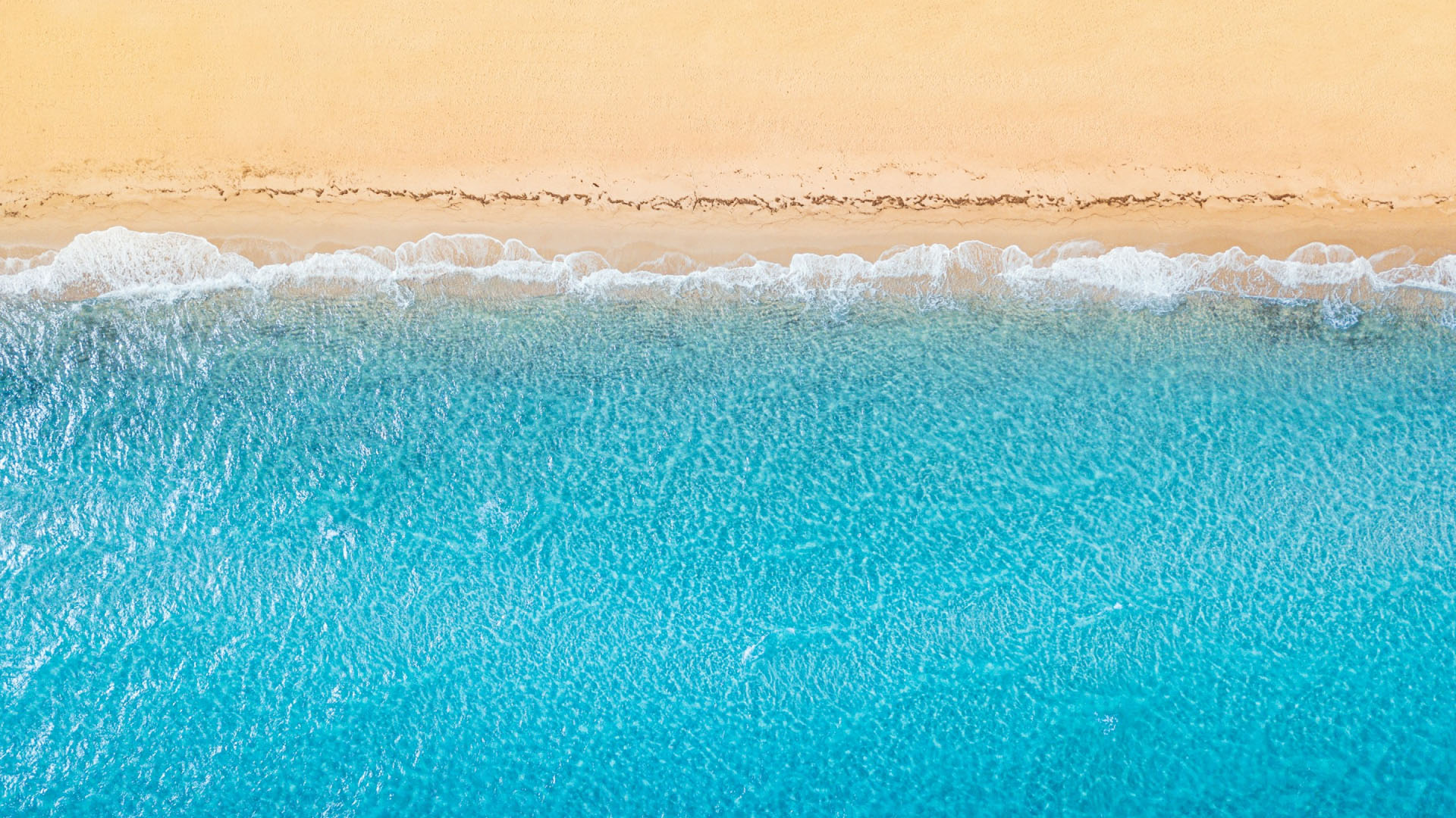 Aerial top-down view of turquoise waves lapping a golden sandy beach.